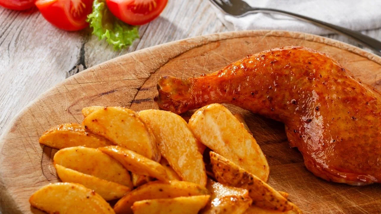 Udka pieczone z ziemniakami leżą na drewnianej tacy.