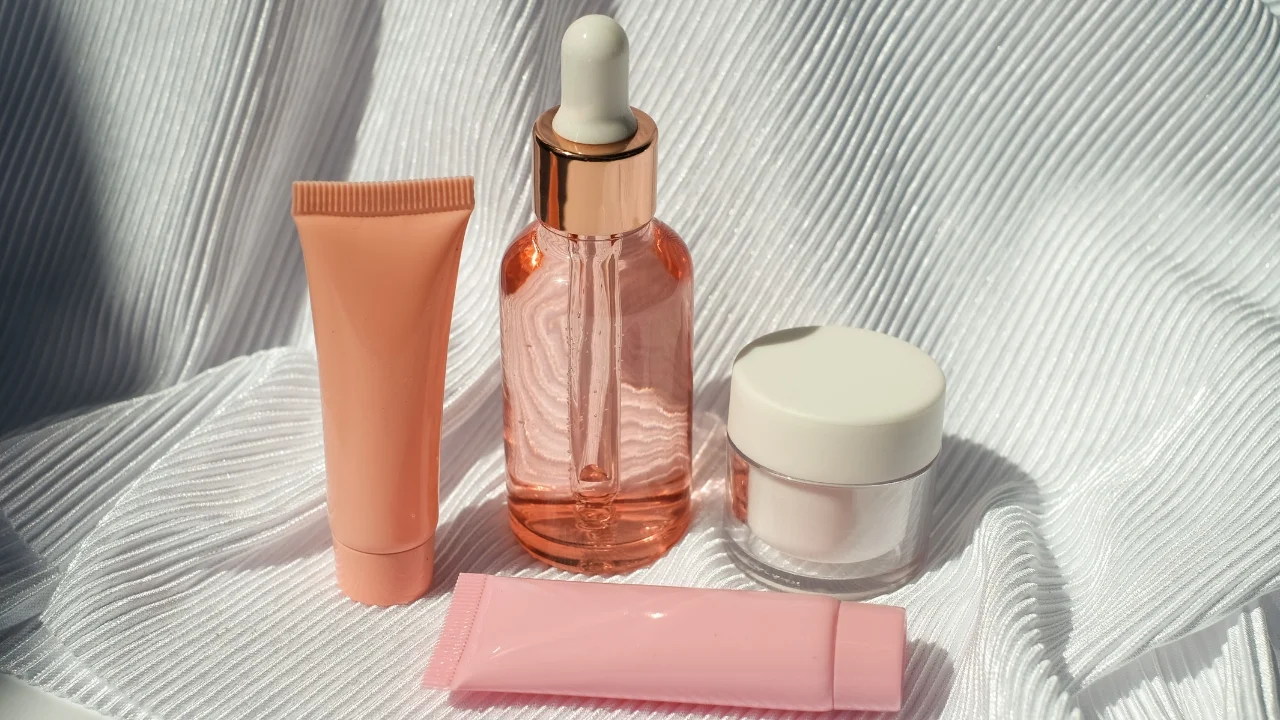 Serum w różowej buteleczce w otoczeniu innych kosmetyków na jasnym tle